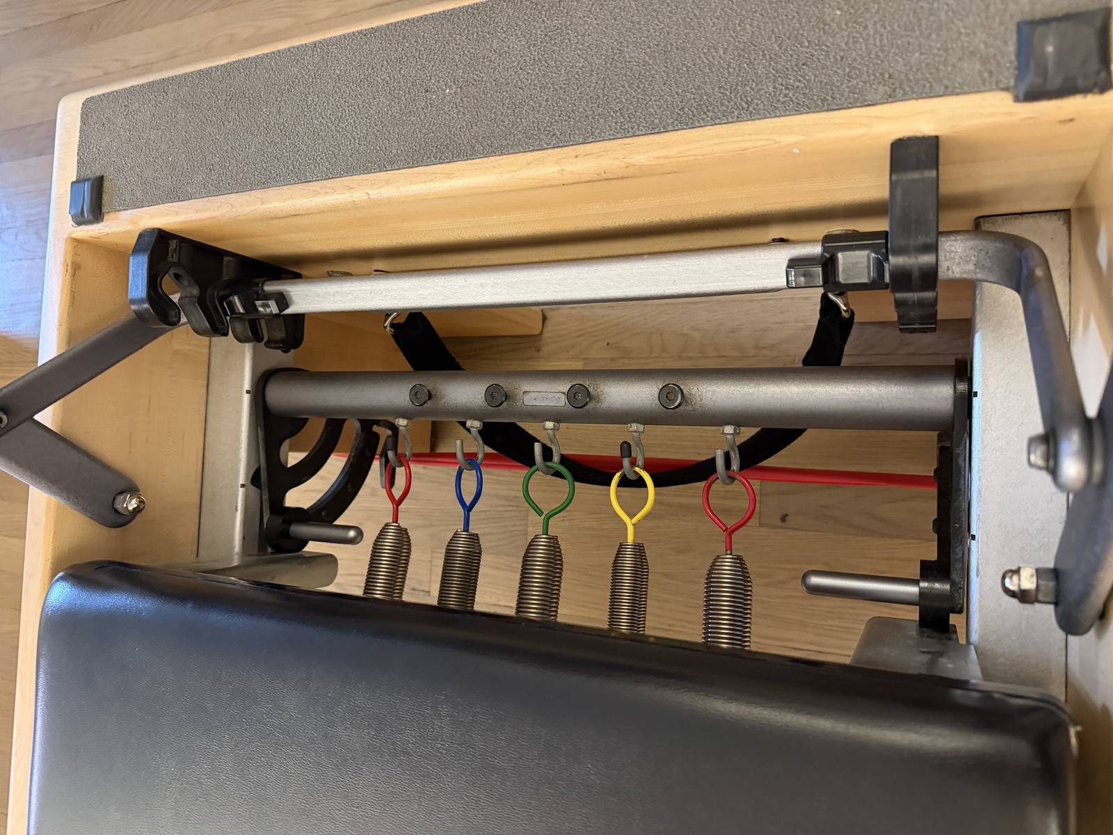 Close-up of a Pilates reformer's color-coded springs and carriage hardware